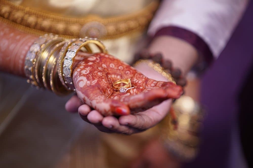Two engagement rings resting on Shravya's hennaed palm, cradled in Pramod's hand